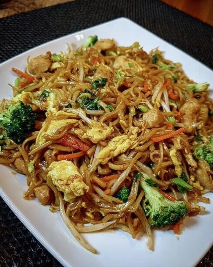 Chinesisch gebratene Nudeln mit Hühnchen, Ei und Gemüse auf einem Teller