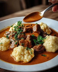 Rahmgulasch mit Serviettenknödeln auf einem Teller serviert.