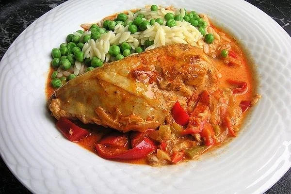 Paprika-Sahne-Hähnchen in einer Pfanne mit frischen Zutaten garniert.