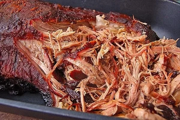 Zartes pulled pork auf einem Brötchen, serviert mit BBQ-Sauce und Krautsalat.